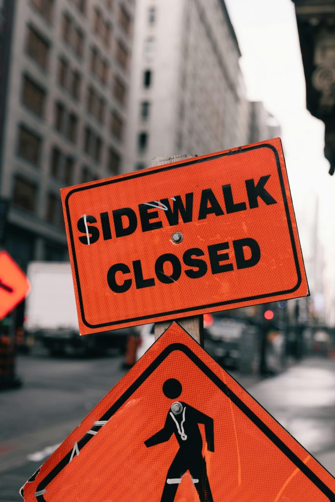 Bright orange 'Sidewalk Closed' sign in a busy city street, emphasizing urban construction.